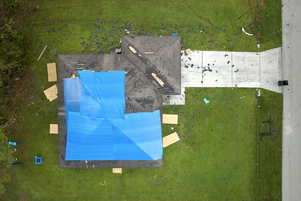 Aerial view of urban roof under emergency tarp — the staging logistics, urgent flashing repairs, and multi-permit coordination that define the day-to-day reality of Hudson County roofing work.