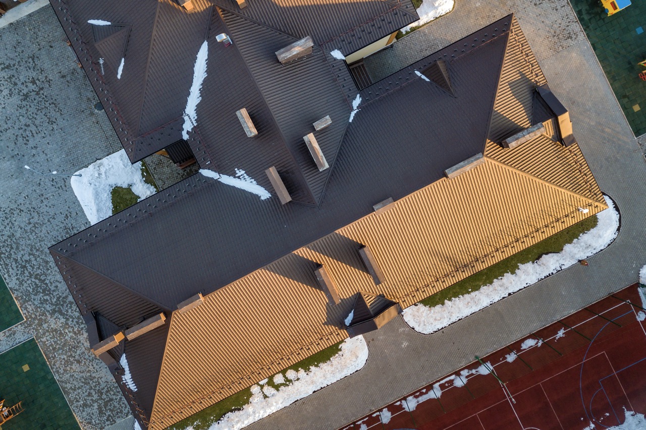 Overhead view of a completed hipped roof with dark brown and tan sections, surrounded by paved courtyards.