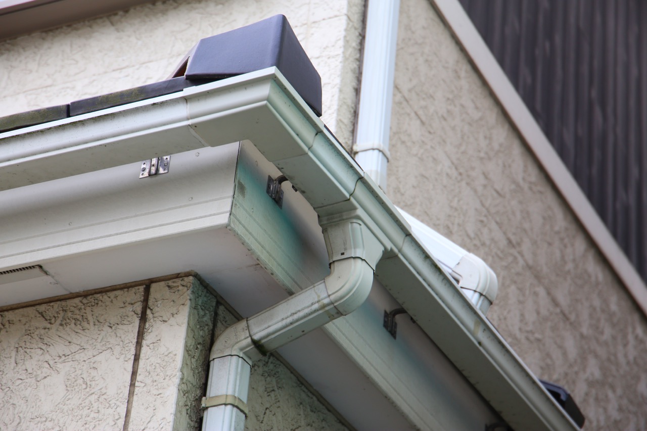 White rain gutter and downspout elbow at the corner of a roof eave on a stucco home.