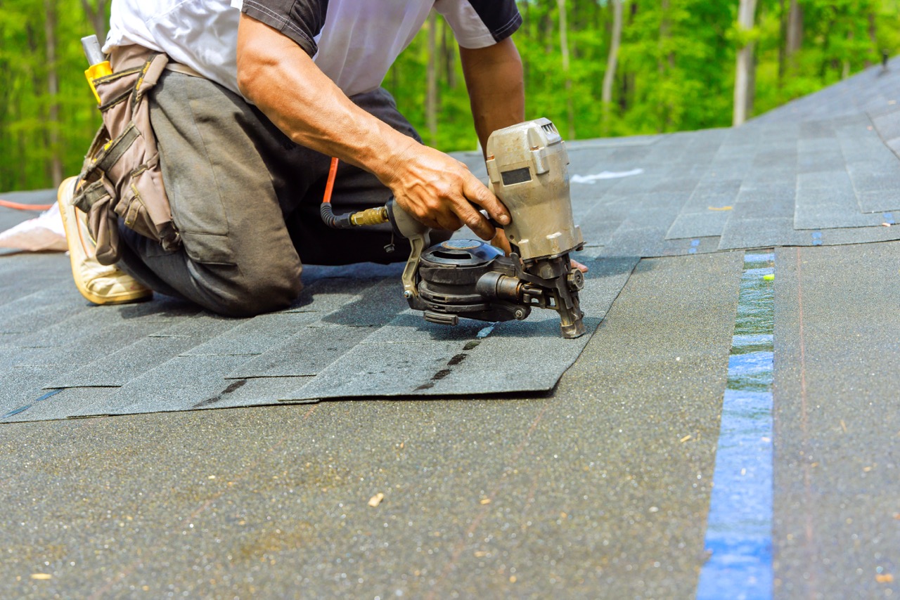 A roofing contractor hand-installing asphalt shingles on a tight-lot urban home — Newark-style staging.