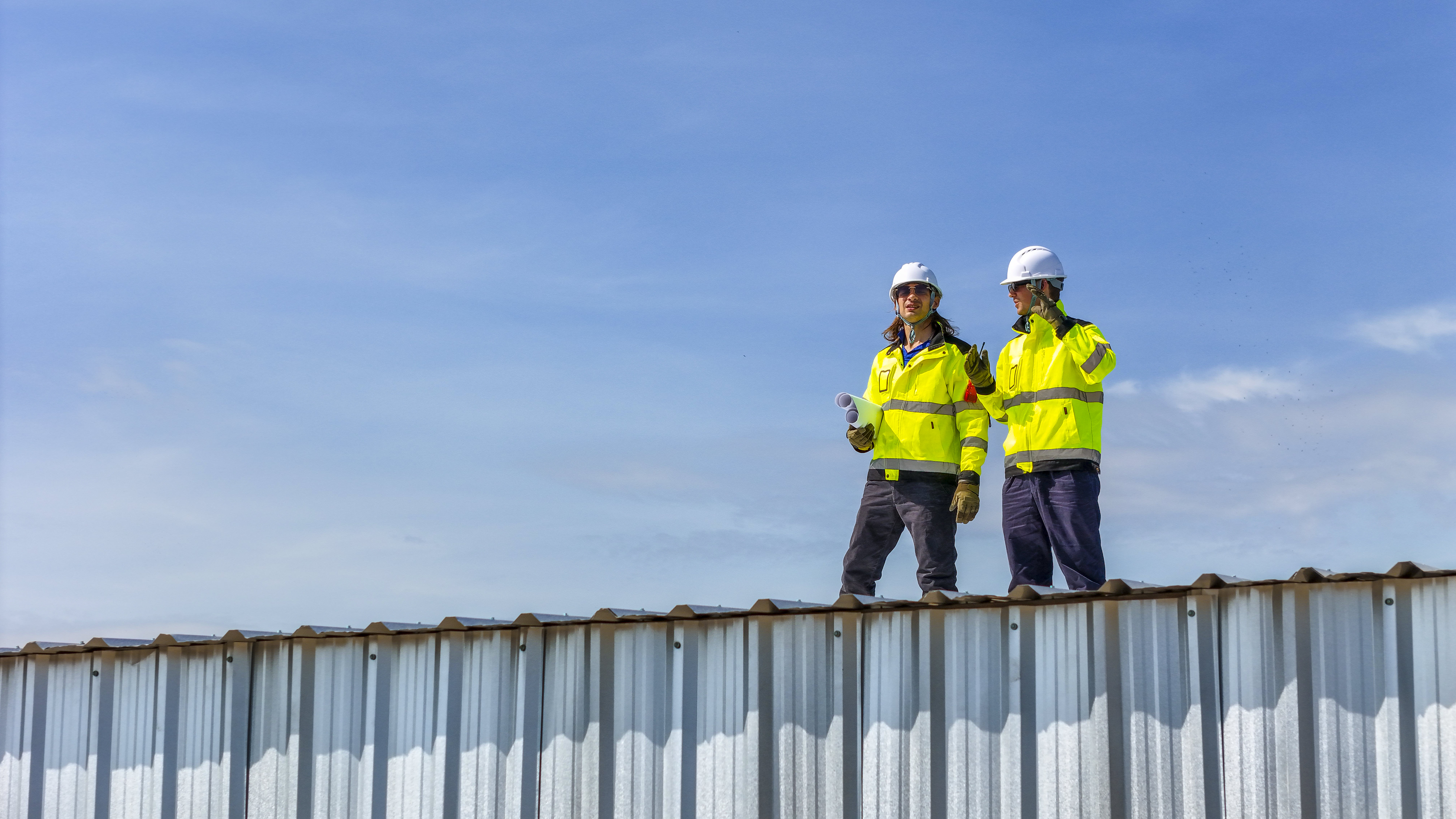 Two NJ-licensed Craftsman Roofing crew members standing on a corrugated metal roof during installation.